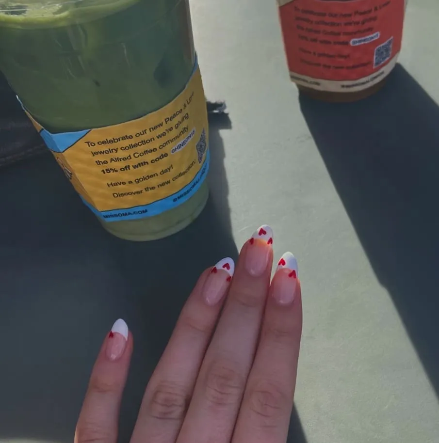 Valentine's French tip nails with tiny red hearts on white tips, beside two juice bottles