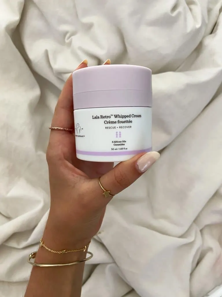 Hand holding a jar of Drunk Elephant Lala Retro Whipped Cream with a lavender lid