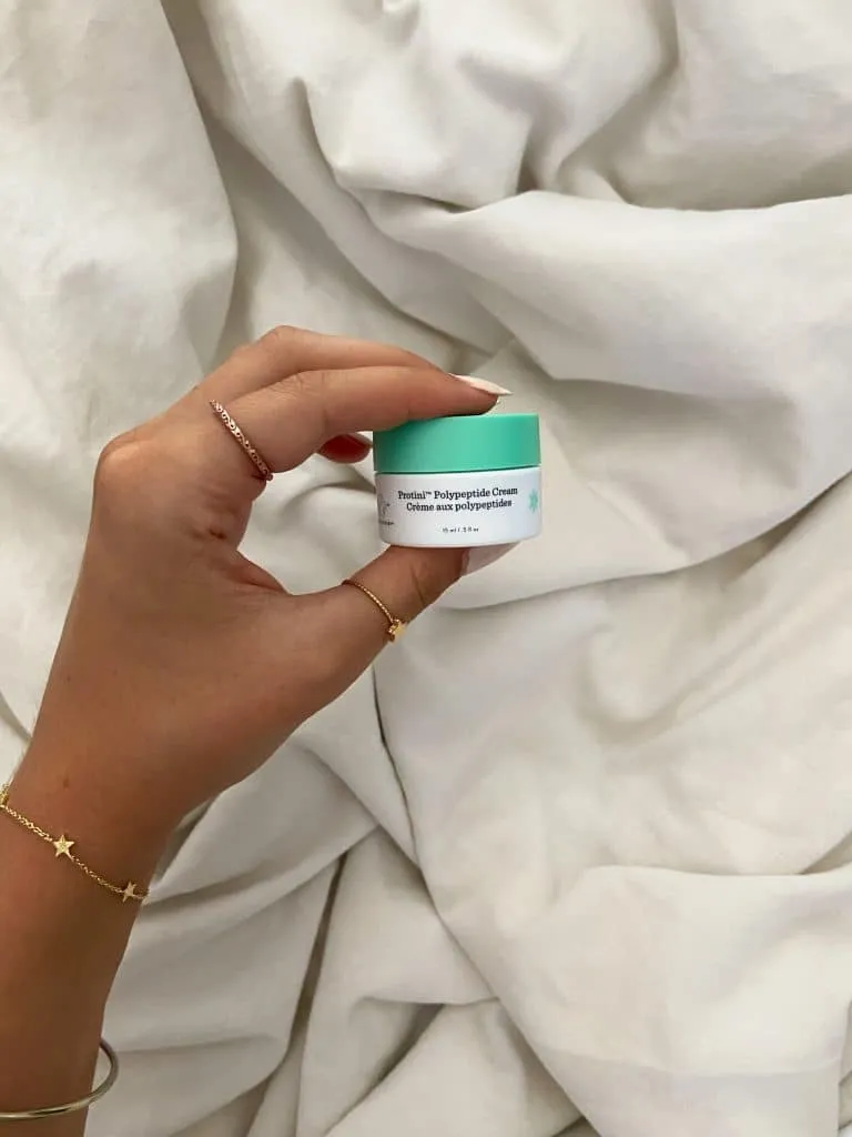 Fingers holding a small mint green jar of Drunk Elephant Protini Polypeptide Cream