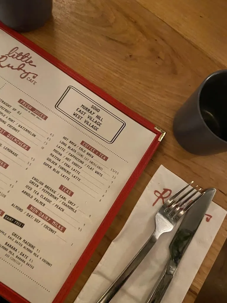Little Ruby's Cafe menu with coffee and juice options, napkin and cutlery on a wooden table