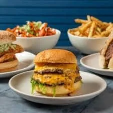 Double cheeseburger with melted cheese, fried chicken sandwich and fries on a blue table