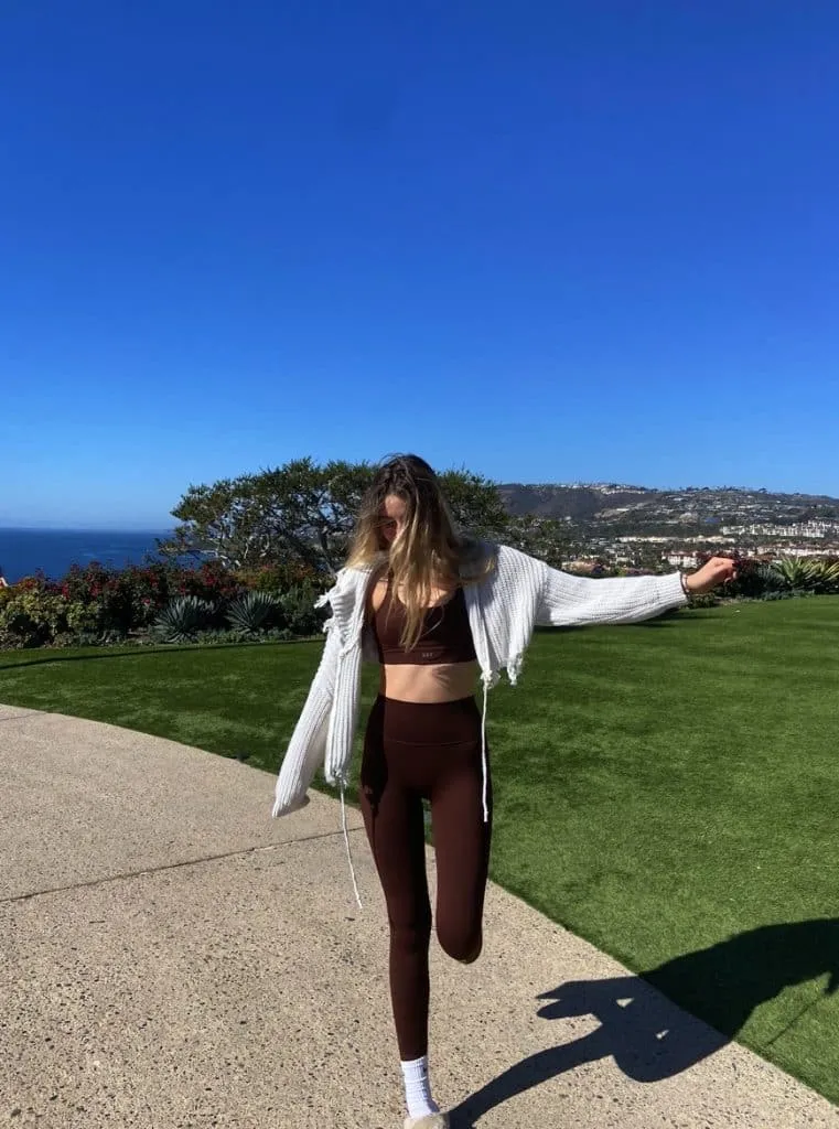 Sky in a chocolate brown Set Active set under a cropped white cardigan on a coastal overlook