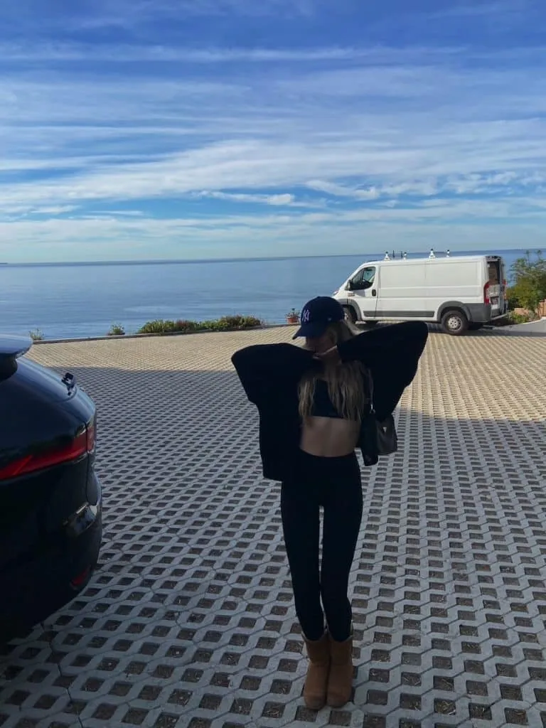 Sky in a black Set Active set, open black hoodie, Yankees cap and UGG boots posing by the ocean