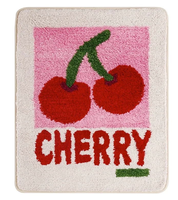 White bath mat with a pink square, two red cherries and the word CHERRY