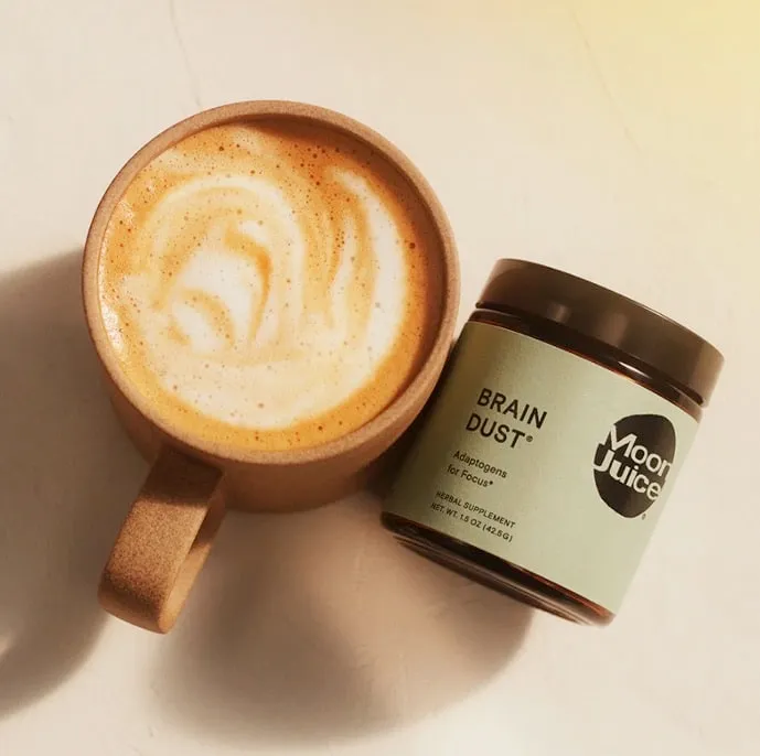 Moon Juice Brain Dust jar beside a brown ceramic latte mug