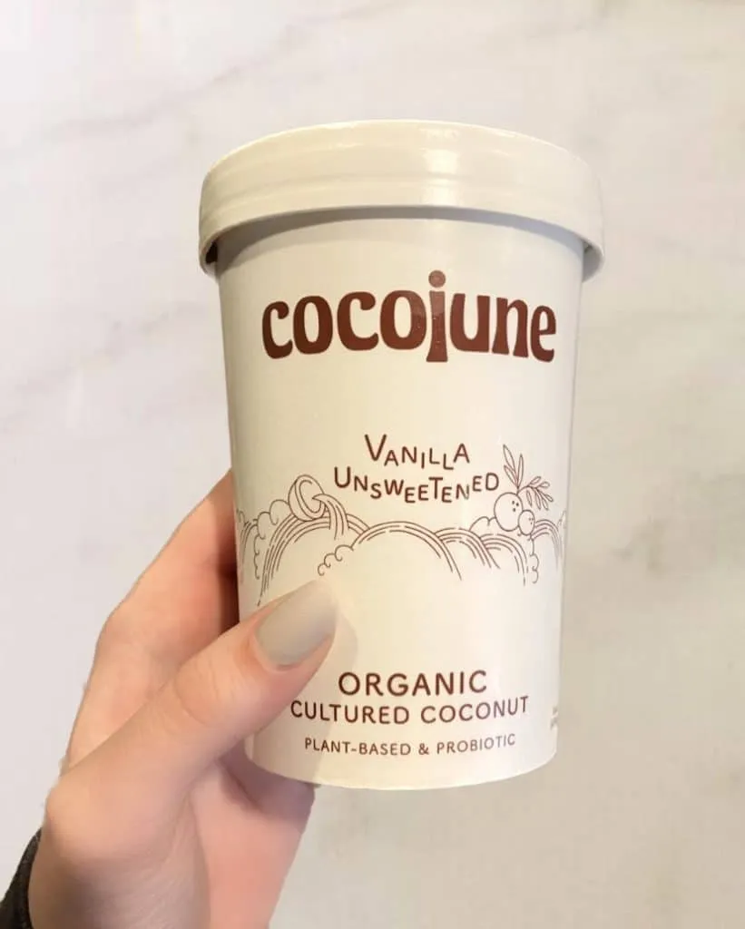 Hand holding a tub of Cocojune vanilla unsweetened organic cultured coconut yogurt