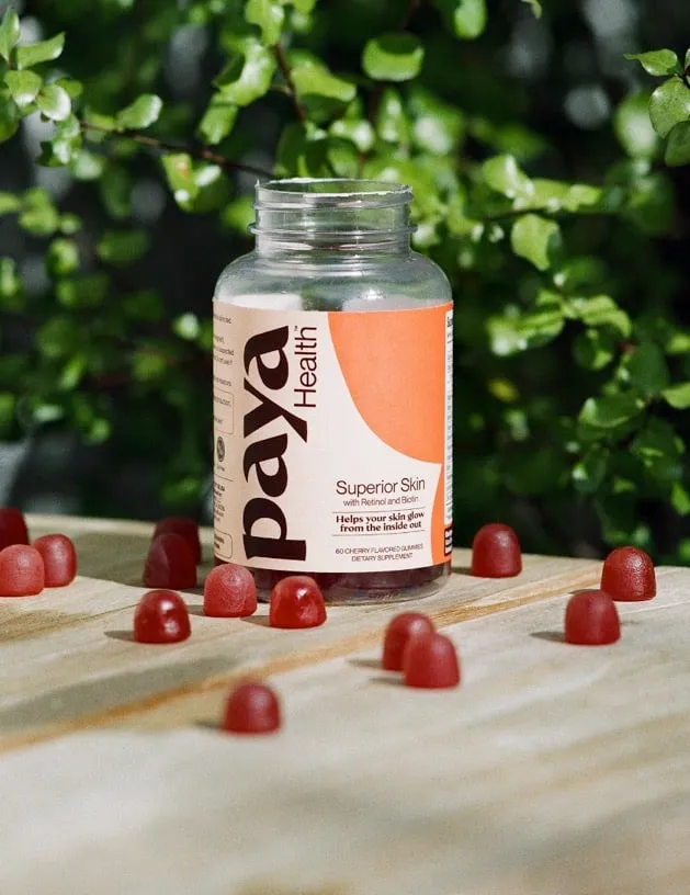 Bottle of Paya Health Superior Skin gummies with red gummies scattered on a wood table