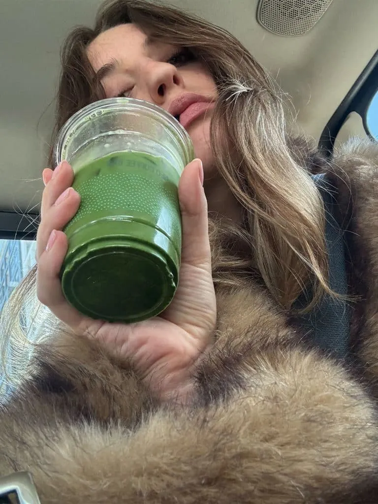 Iced matcha latte with oat milk from NEO Coffee Bar, held up by a girl in a fur coat