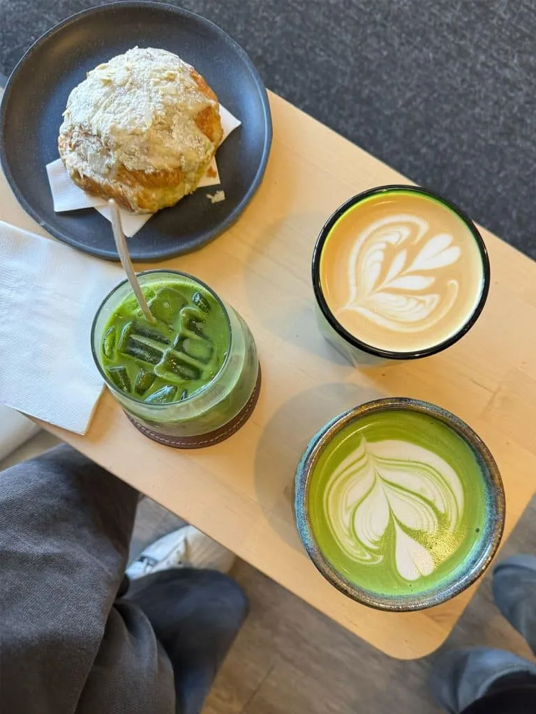 Overhead view of an iced matcha, two hot matcha lattes with latte art in ceramic cups and a pastry at Ninetails Coffee on Bloor