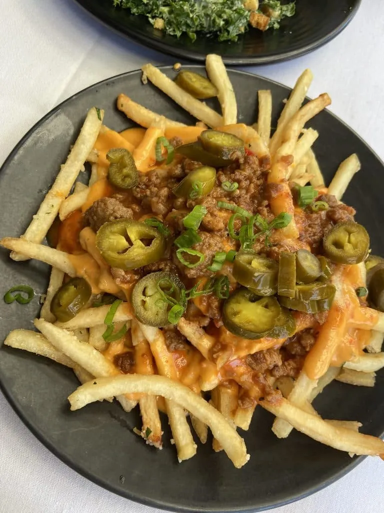 Loaded fries with cheese sauce, seasoned meat, jalapeños and green onions on a black plate at Crossroads Kitchen
