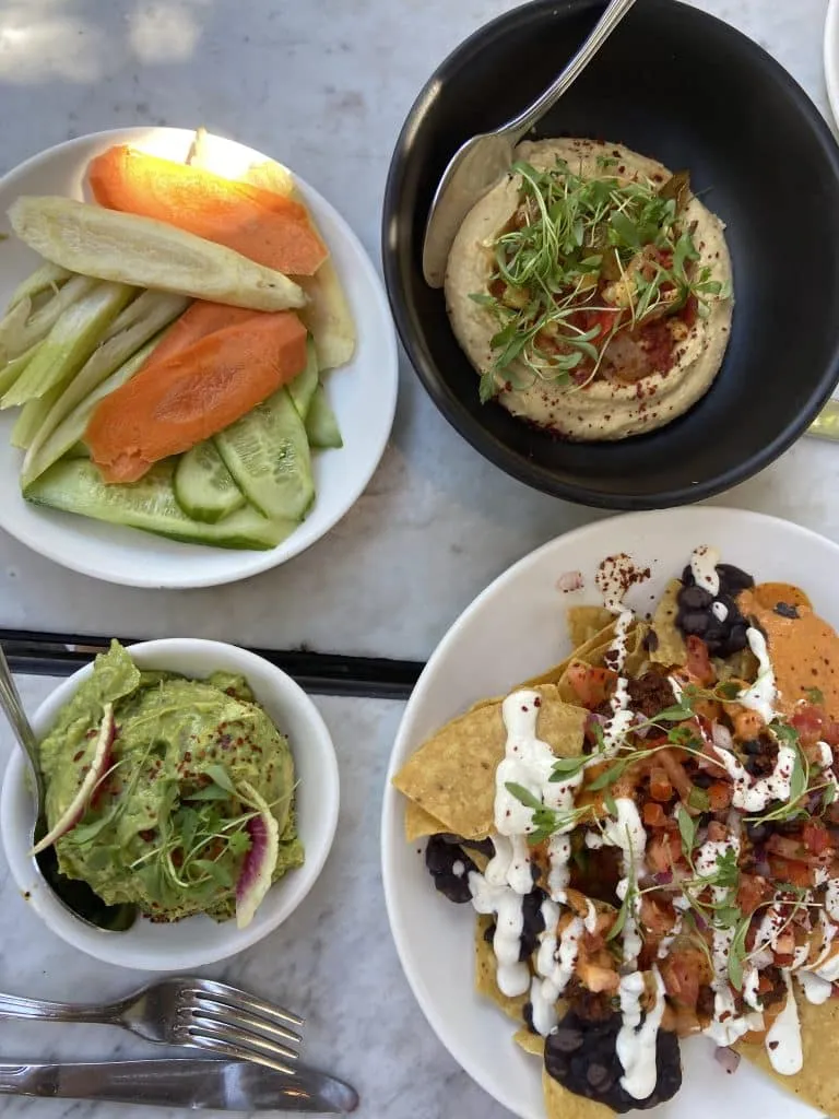Overhead at Gracias Madre: crudités, hummus, guacamole and loaded nachos on a white marble table