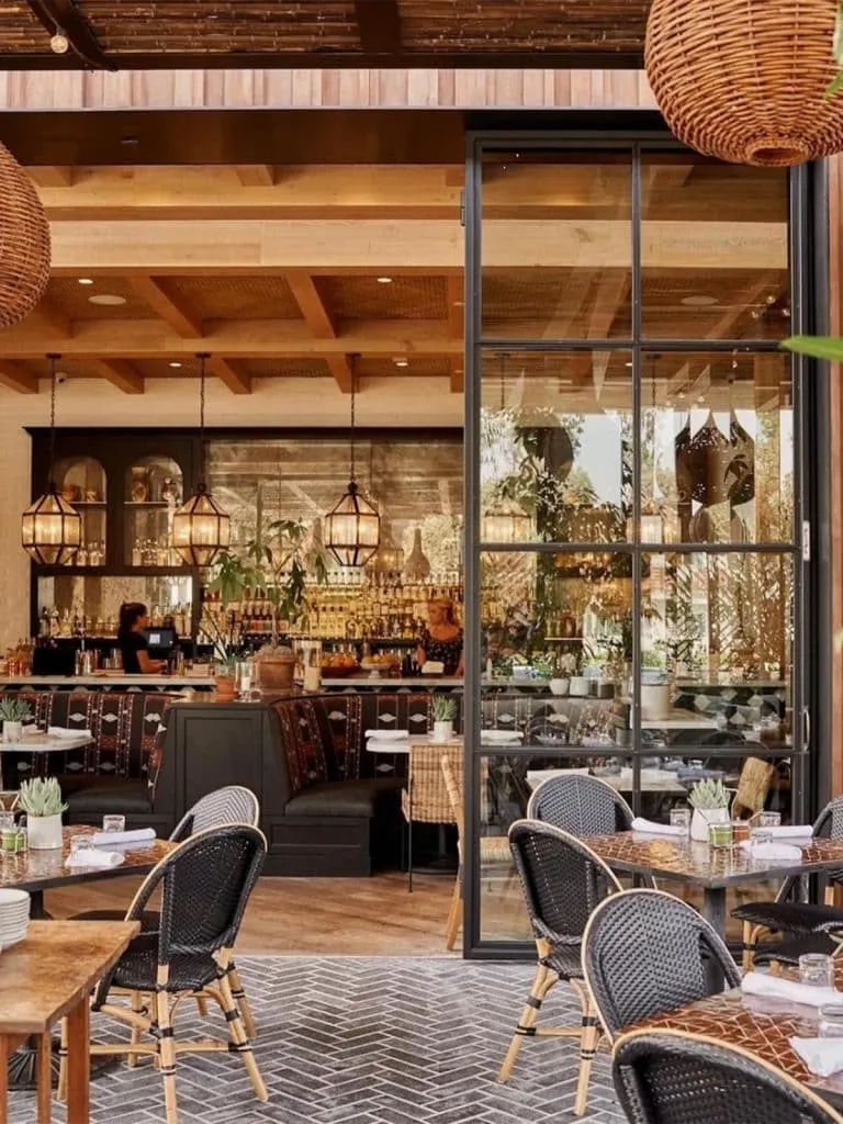 Gracias Madre patio with woven bistro chairs looking into a warm bar lit by gold lanterns