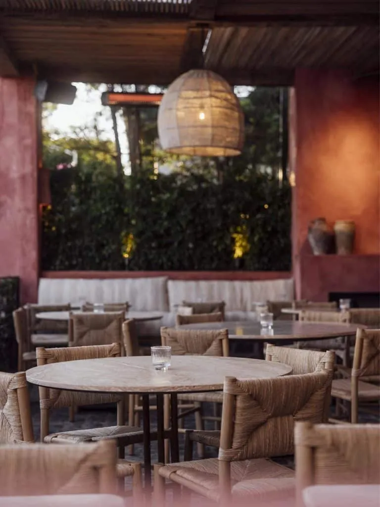 Outdoor patio at Great White with woven chairs, round tables, a large pendant light and a wall of greenery