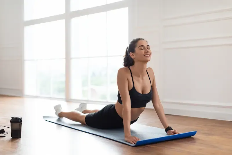 Smiling woman stretching on a blue yoga mat in a bright studio with large windows