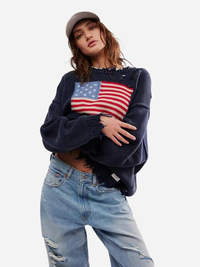 Model in the Free People Denimist Flag Sweater, a distressed navy knit with an American flag, and ripped jeans
