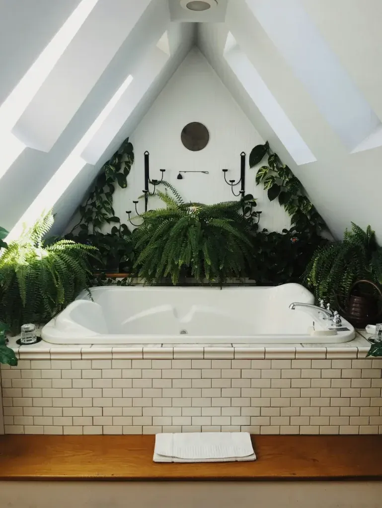 Attic bathroom with a white tub, white subway tiles, a wooden floor and lush ferns and trailing plants