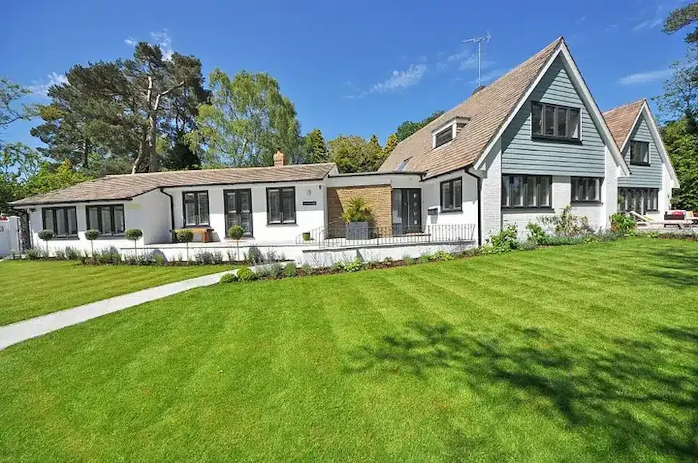 White and grey house with gabled roofs and a large freshly mowed green lawn under a blue sky