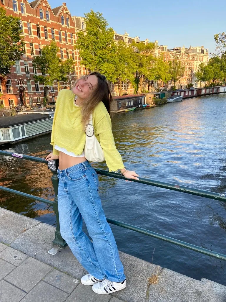 Girl in a yellow cardigan and baggy jeans leaning on a railing by an Amsterdam canal