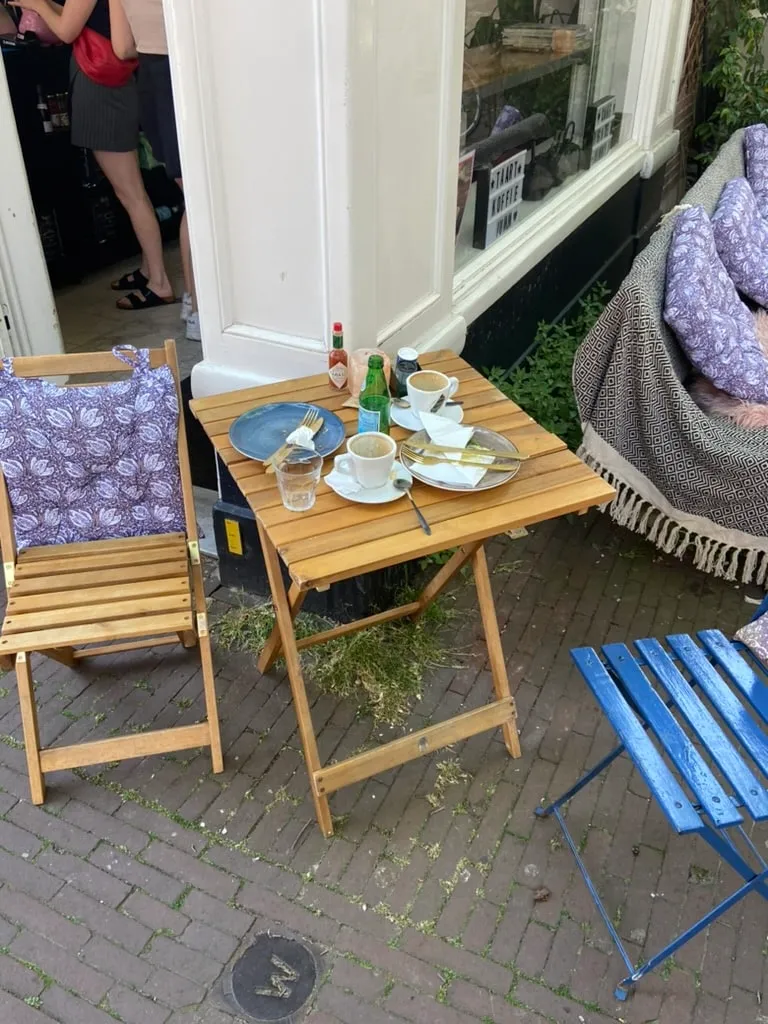Wooden folding cafe table with coffee cups and a blue chair on an Amsterdam sidewalk