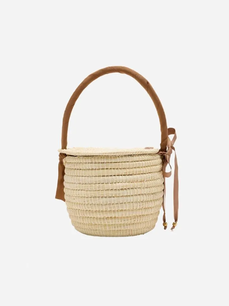 Cream woven straw bucket bag with a tan fabric handle, ribbon ties and gold bead ends