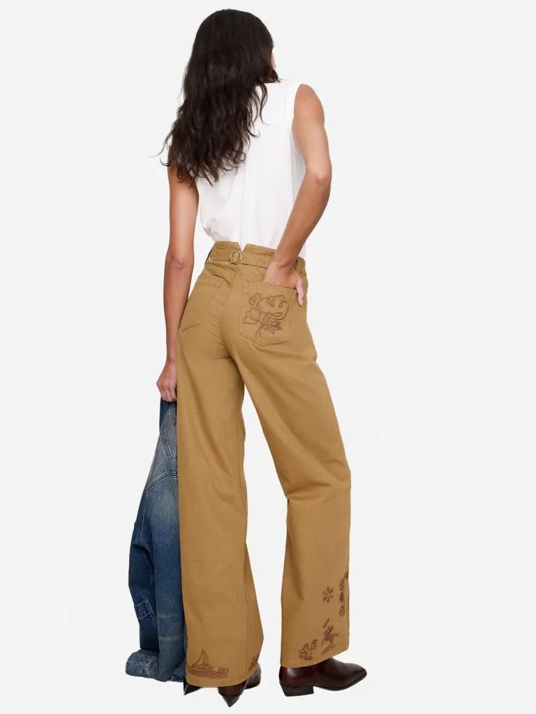 Back view of a model in tan embroidered relaxed-straight canvas pants with a white tank and brown boots