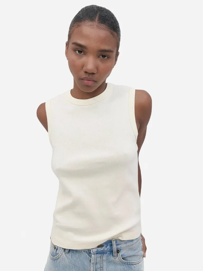 Model in a cream sleeveless knit undershirt tucked into light-wash jeans