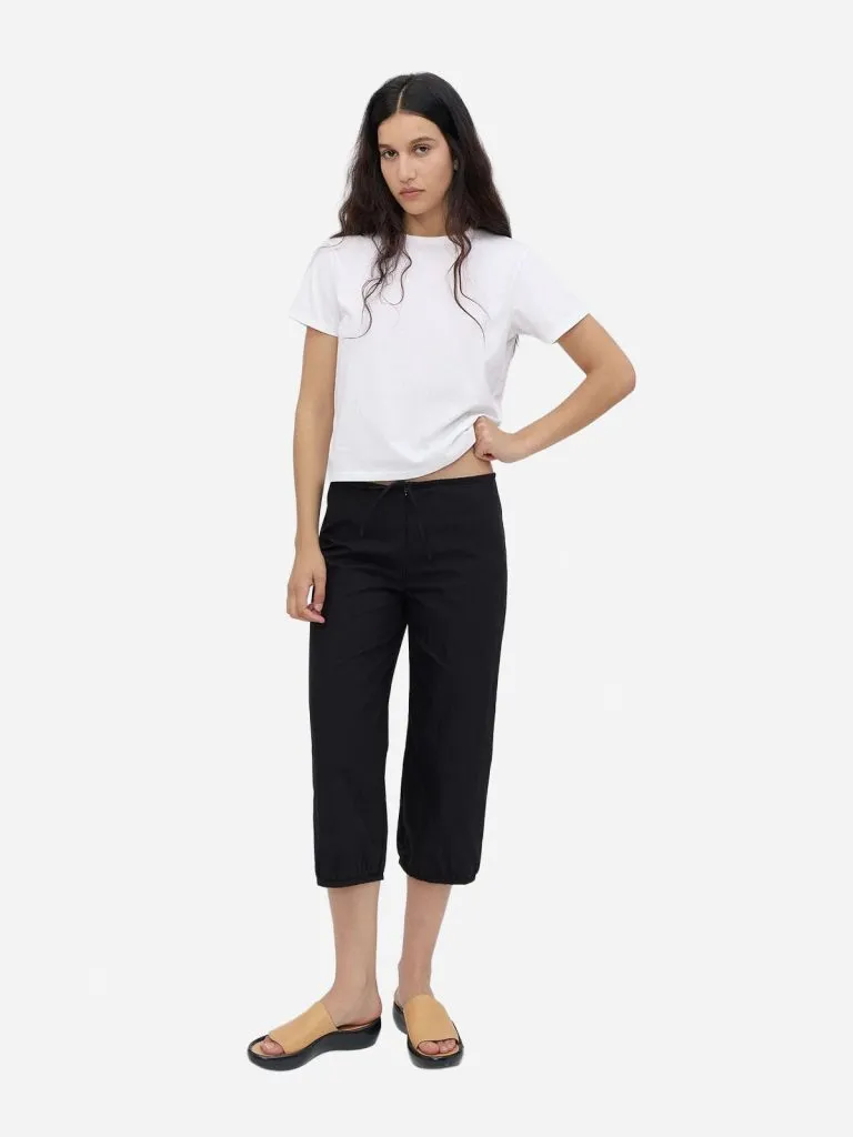 Model in black cropped pants with gathered hems, a white tee and tan sandals