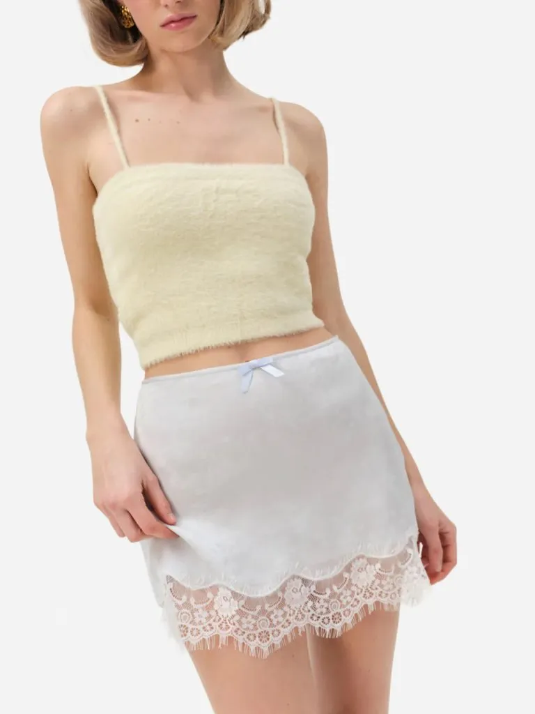 Model in a cream fuzzy knit tank with thin straps over a white satin skirt with a lace hem