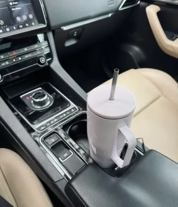 Lilac Corkcicle tumbler with a metal straw sitting in a car cupholder next to the gear shifter