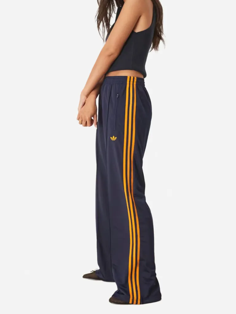 Navy Adidas track pants with orange side stripes and a yellow trefoil logo, worn with a black crop top
