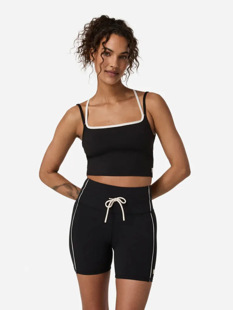 Woman in a black cropped tank with white piping layered over white straps, with matching black biker shorts