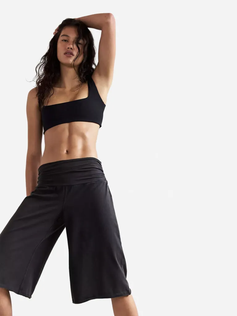 Woman in a black one-shoulder sports bra and black wide-leg Free People Hot Shot pants