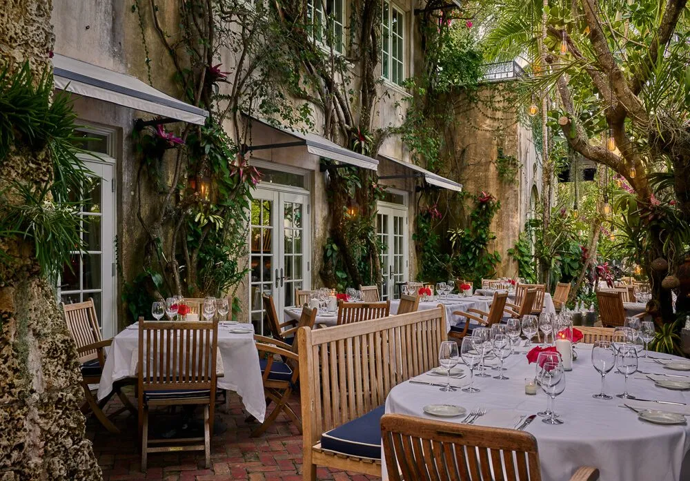 Garden patio at Casa Tua Miami Beach with white tablecloths, teak chairs and vines climbing the walls